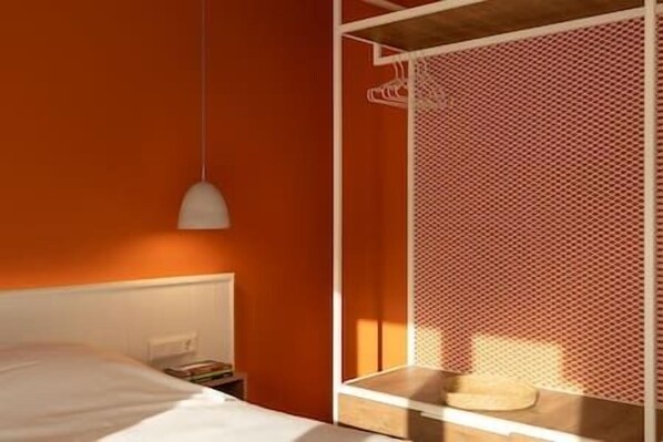 Ein Zimmer mit einem Bett, einem weißen Nachttisch, einer weißen Lampe und einem Holztischchen mit einem Korb.