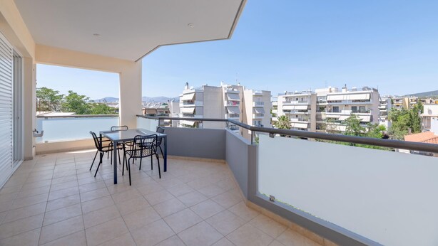 Un balcon avec une table et des chaises, donnant sur une étendue d’eau et des immeubles d’habitation.