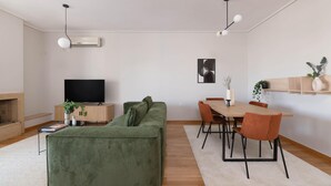 Un salon moderne avec un canapé vert, une table à manger en bois et des chaises orange, un téléviseur à écran plat et une cheminée.