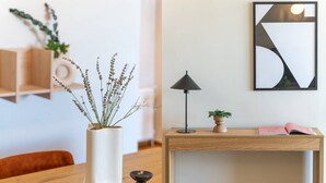 Une table en bois sur laquelle se trouve un vase blanc contenant des plantes séchées, une lampe noire, une petite plante en pot et un livre rose, le tout posé sur une petite table d’appoint en bois.