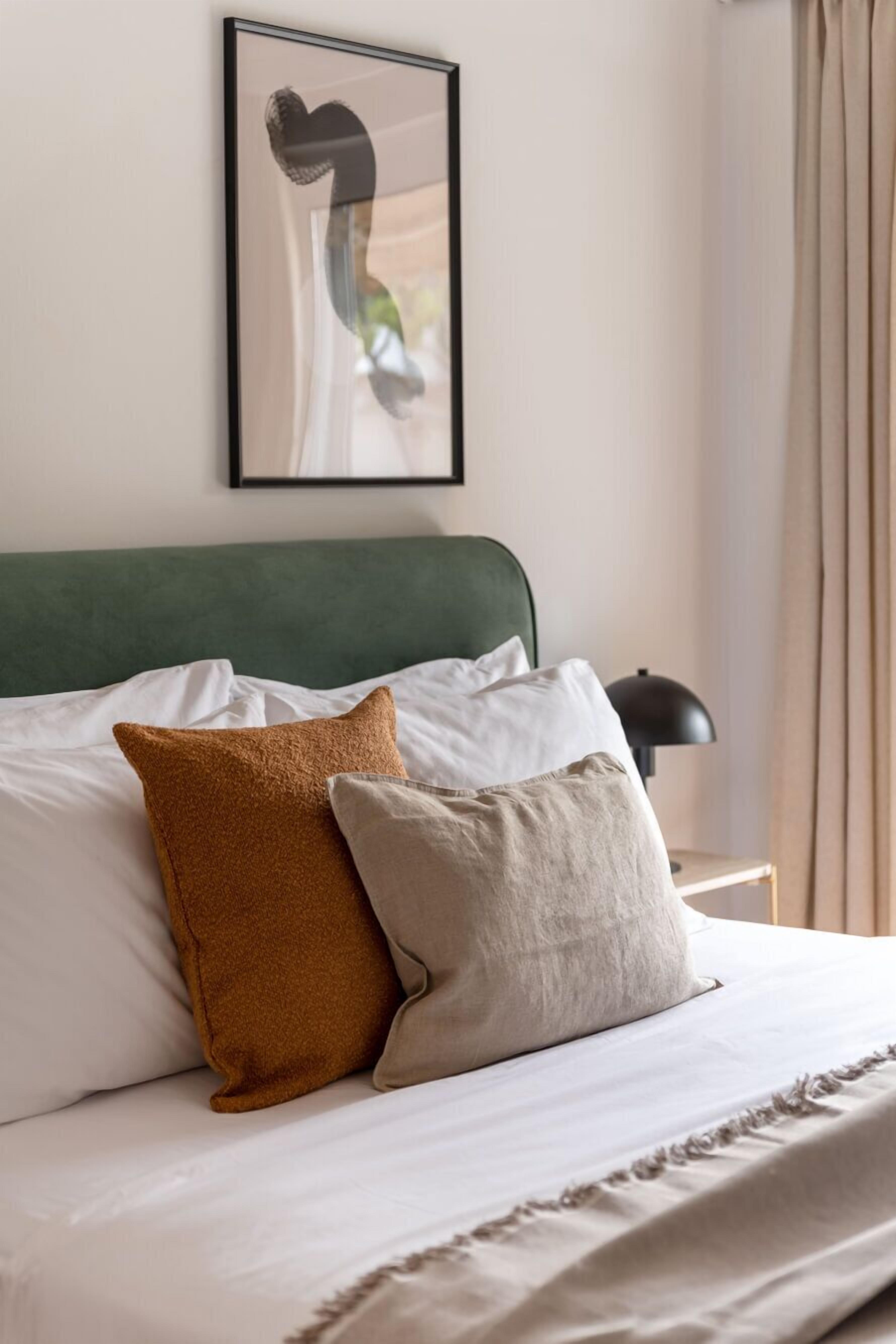 A neatly made bed with a green headboard, two pillows, and a framed artwork above it.