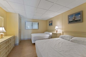 A hotel room with two beds, a dresser, a window, and a painting on the wall.