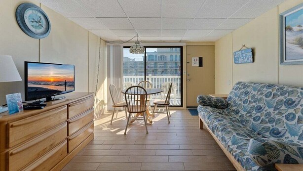 Ein Zimmer mit Fernseher auf einer Holzkommode, einer Couch mit gemustertem Bezug, einem Esstisch mit Stühlen und Blick durch eine Glastür.
