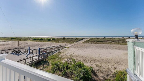 Une vue sur la plage avec une promenade en bois menant à l’eau, un ciel dégagé et un horizon lointain.