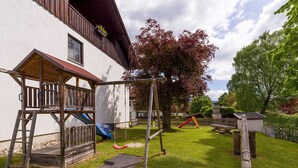 A playground with a swing set, slide, and climbing structure, surrounded by a well-maintained lawn and trees. - Vacation apartment Schanzenblick C8 (Oberaudorf)
