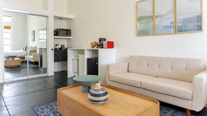 Een moderne woonkamer met een beige bank, een houten salontafel en een keuken op de achtergrond.