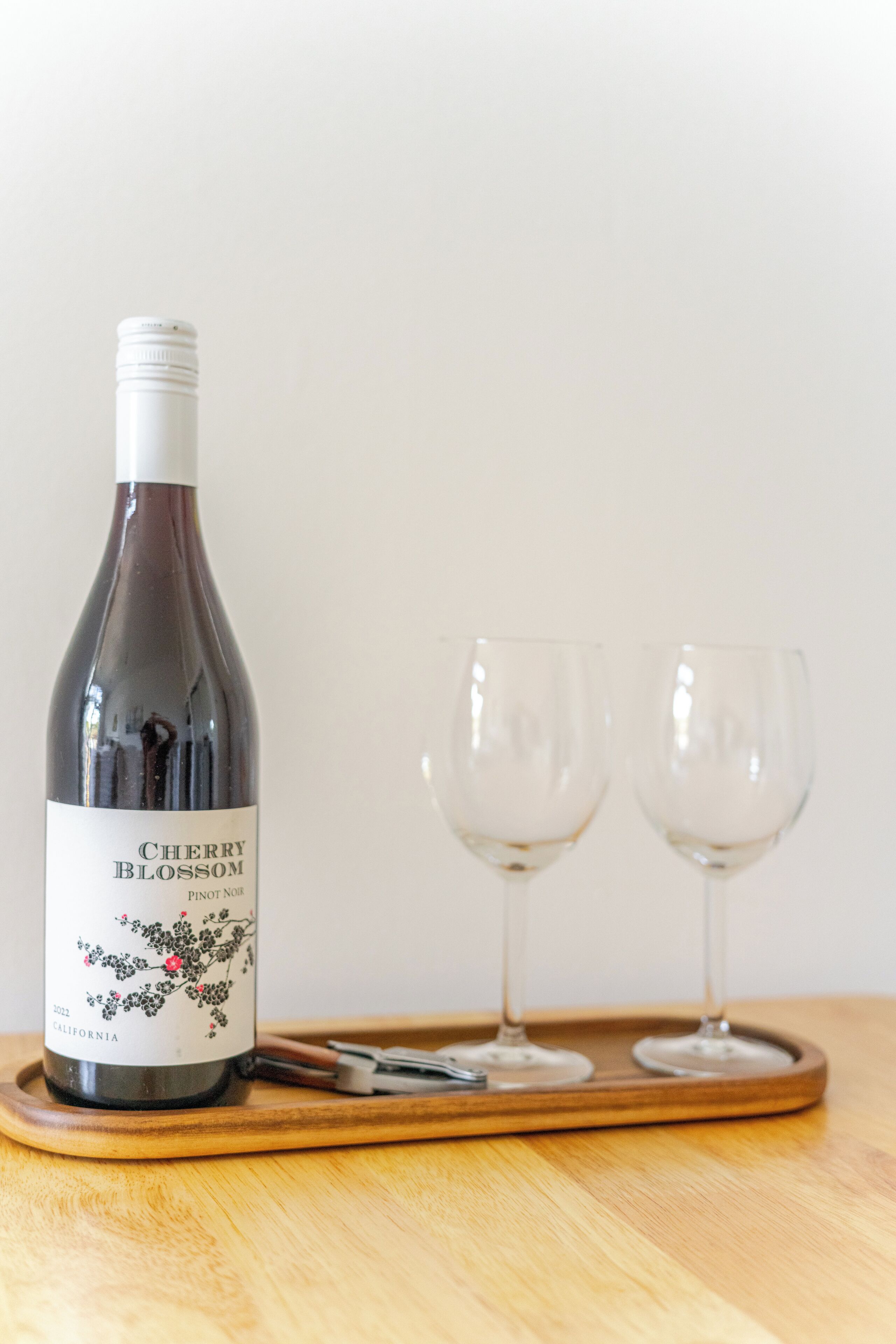 En flaske Cherry Blossom Pinot Noir vin på en træbakke med to tomme vinglas.
