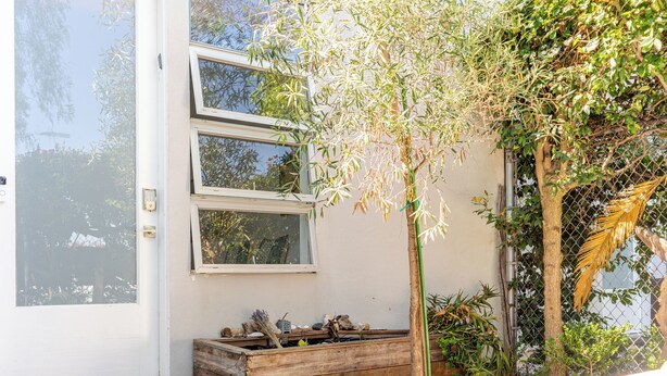 Een modern gebouw met grote ramen, een houten bankje en een kleine boom op de voorgrond.