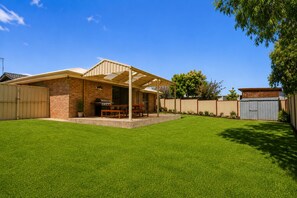 A backyard with a barbecue area, a brick house, and a fenced yard. - Family Oasis At Busselton (Geographe)