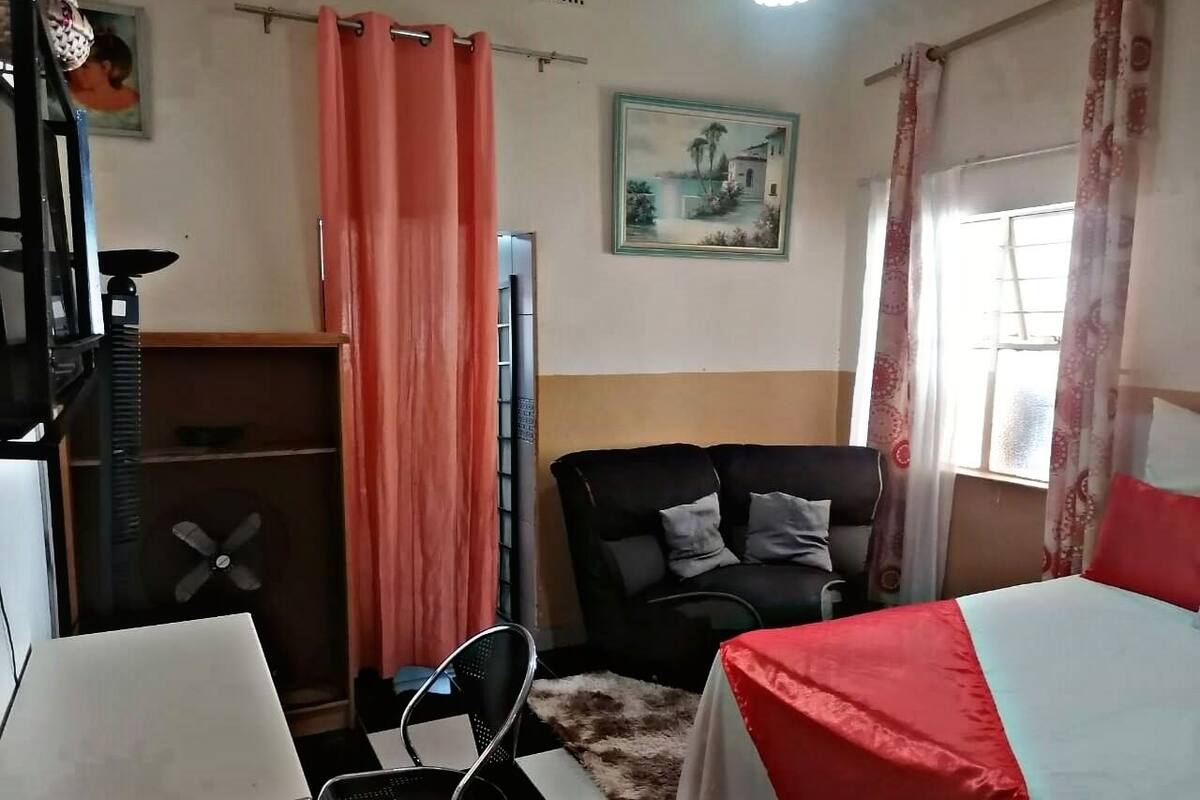 Une pièce comprenant un lit, un bureau, une chaise, un canapé et une fenêtre avec des rideaux.