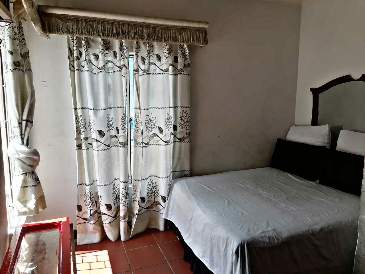 Un dormitorio con cama, ventana con cortinas y puerta.