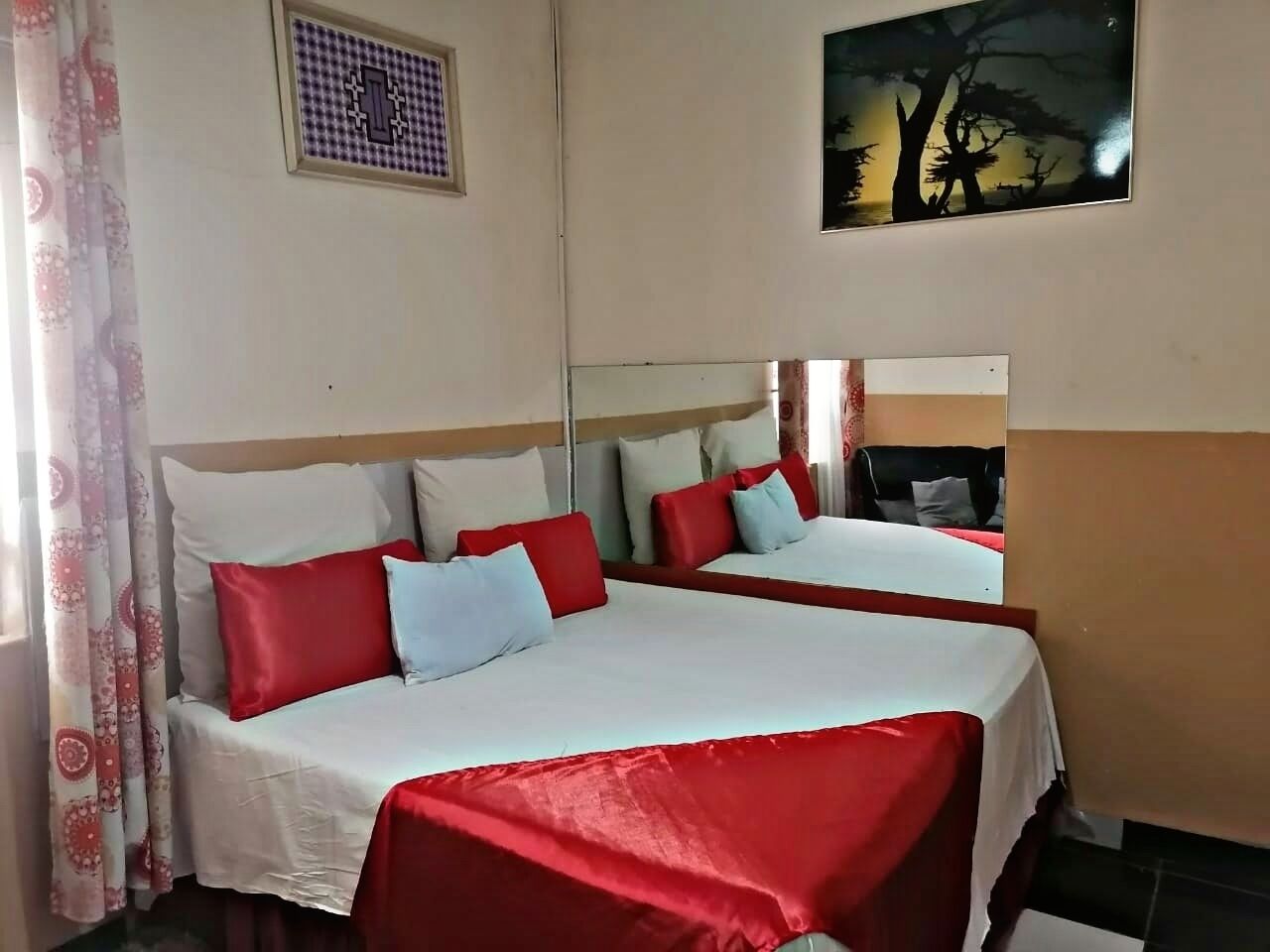 Habitación de hotel con dos camas, cada una con ropa de cama roja y blanca, cabeceros y un cuadro en la pared.