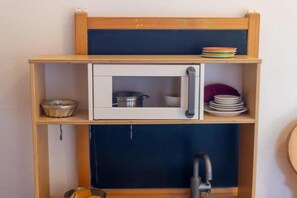 Une petite cuisine équipée d’un four à micro-ondes, d’un évier et d’une étagère où sont rangés la vaisselle.