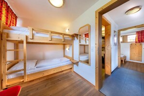 Une chambre avec un lit superposé, un plancher en bois, un miroir et une porte donnant sur une autre pièce.