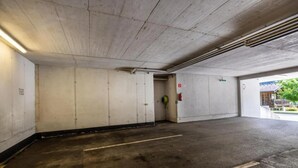 A parking garage with concrete walls, a fire extinguisher, and a fire hose on the wall.