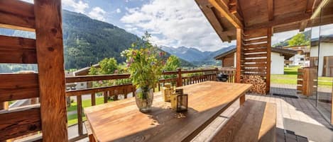 Una terraza de madera con una mesa y bancos, con vistas a un paisaje montañoso.