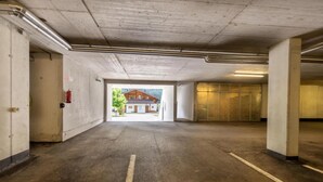 An underground parking garage with concrete pillars, a fire extinguisher on the wall, and a view of a building outside.