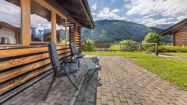 A wooden cabin with a patio area featuring outdoor seating and a view of a mountainous landscape.