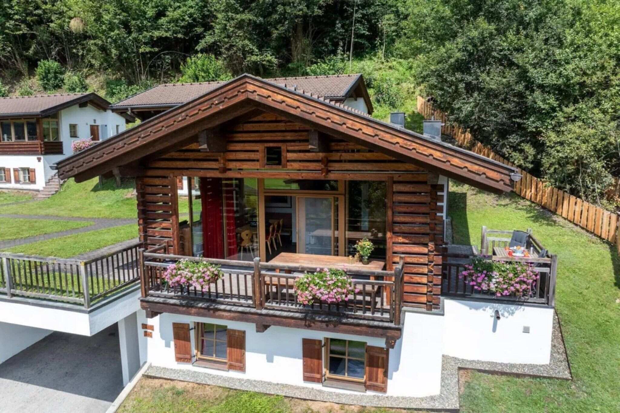 A two-story chalet with a balcony, wooden exterior, and a view of a forested area.