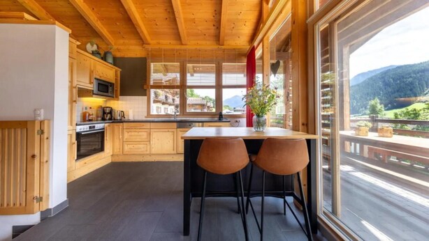 A modern kitchen with wooden cabinets, a central island, and a view of a mountainous landscape.