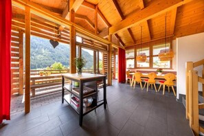 Un intérieur en bois avec une table et des chaises, une vue sur une zone boisée à l’extérieur et un rideau rouge sur le côté gauche.