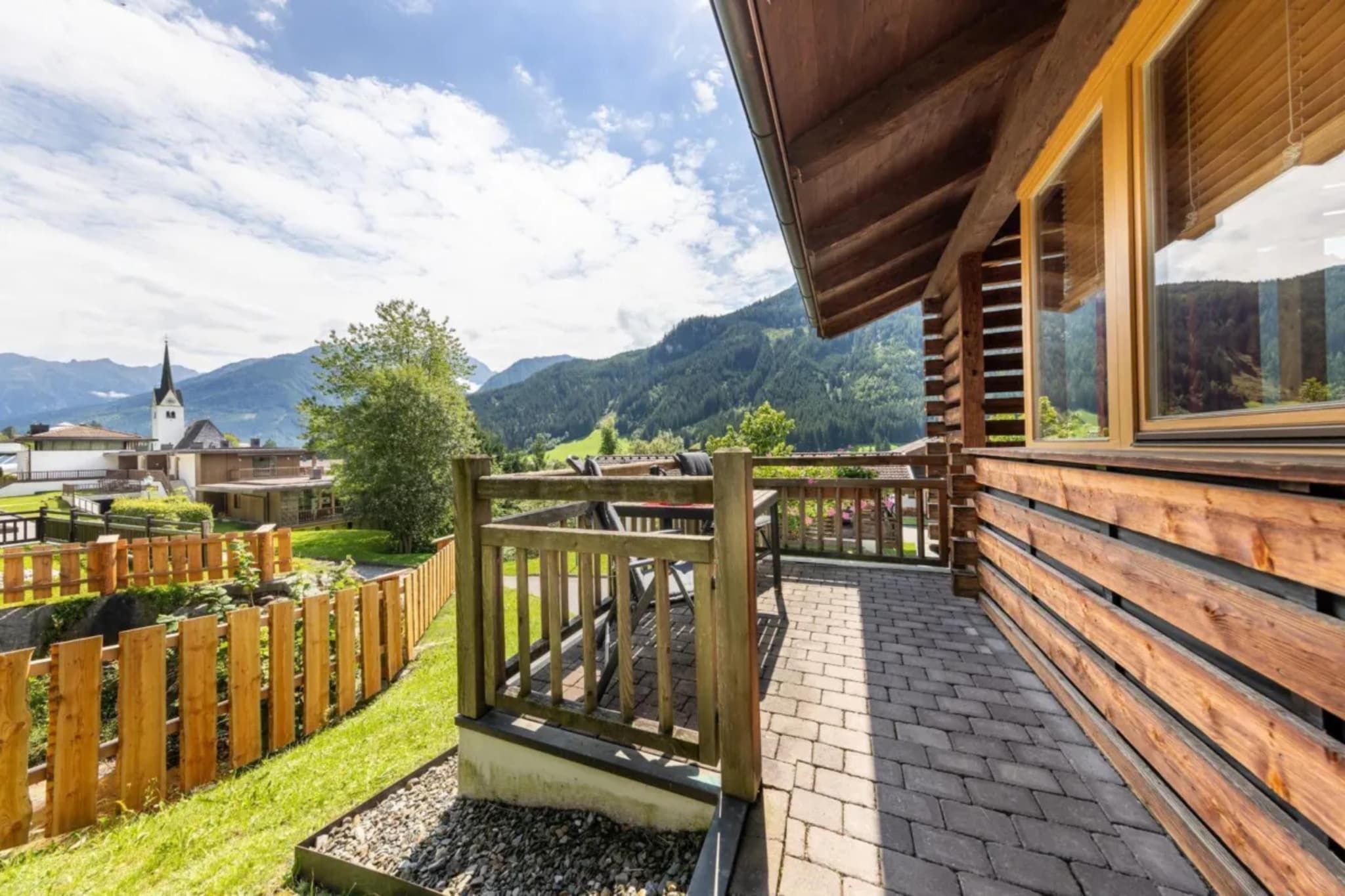Une terrasse en bois offrant une vue sur un paysage montagneux, une église et un ciel dégagé.