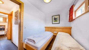 A single-bed room with a wooden headboard, a small bedside table, a wall-mounted picture, and a window with a curtain.