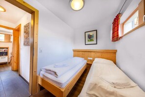 Une chambre avec un lit simple, une tête de lit en bois, une petite table de chevet, un tableau accroché au mur et une fenêtre avec un rideau.