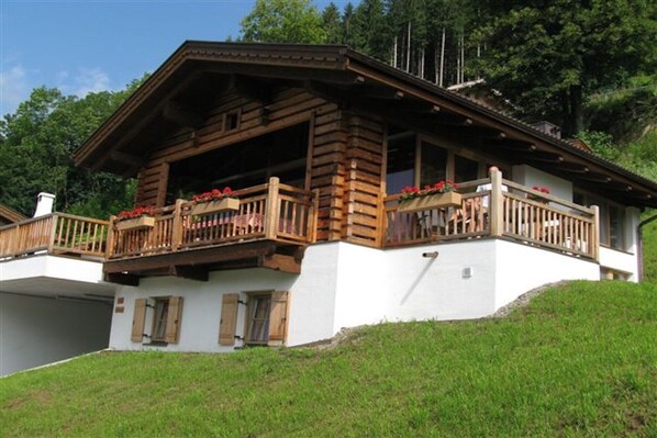 A wooden chalet with a balcony, white walls, and a sloped roof.