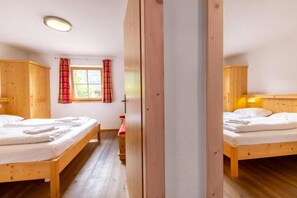 Een kamer met twee houten bedden, een raam met gordijnen en een houten garderobe.