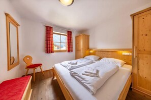 Een slaapkamer met twee bedden, een houten garderobe, een stoel, een raam met gordijnen en een spiegel.