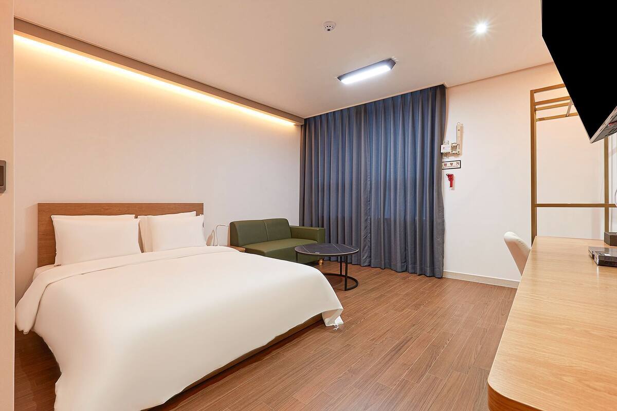 Une chambre d’hôtel avec un lit, un fauteuil vert, une petite table ronde et un bureau en bois.