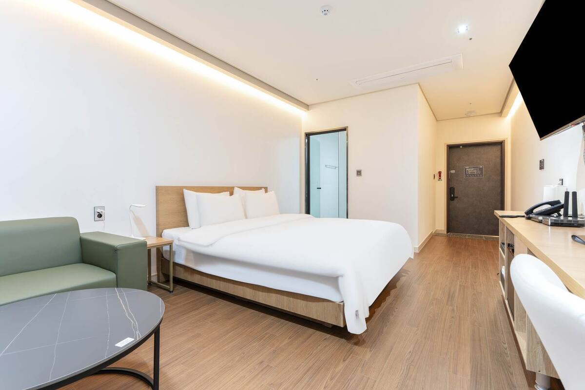 Une chambre d’hôtel moderne, équipée d’un lit, d’un canapé vert, d’un bureau avec un ordinateur et d’un téléviseur fixé au mur.