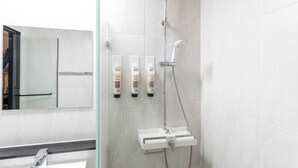 A modern bathroom with a glass shower enclosure, a white sink, and three bottles of shampoo on the wall. - HOTEL DEOKYEONG (Wonju)