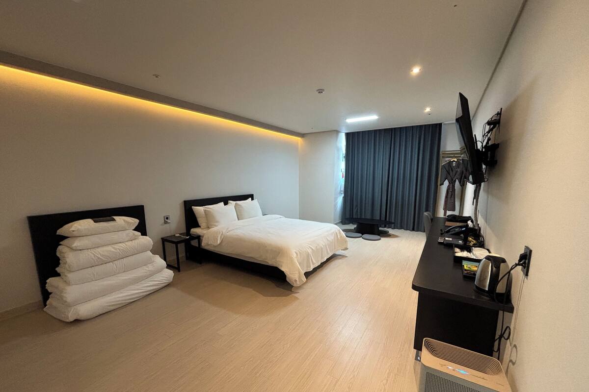 Une chambre d’hôtel moderne dotée d’un grand lit, de tables de chevet, d’un bureau avec une chaise, d’un téléviseur à écran plat et d’une grande fenêtre avec des rideaux.