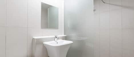 Un baño moderno con un lavabo blanco, un espejo y una cabina de ducha de vidrio.