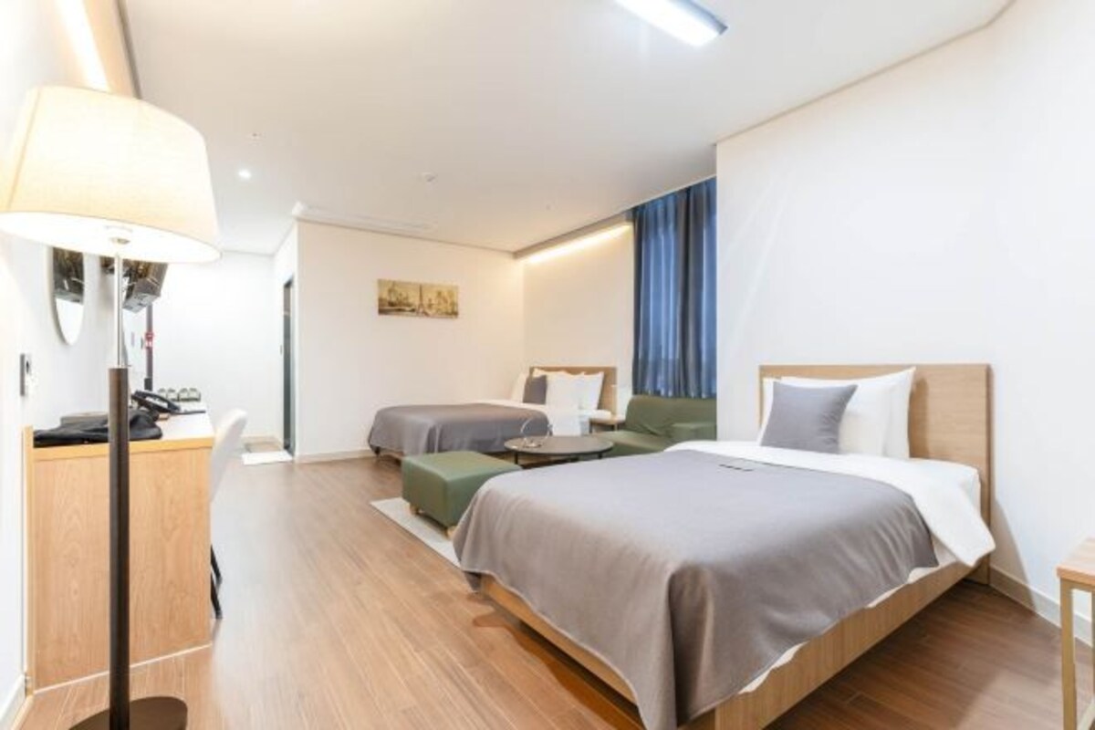 A modern hotel room with a large bed, a desk, a chair, and a sofa.