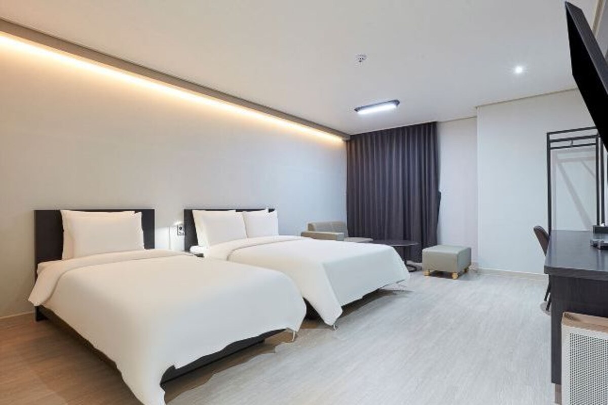 A modern hotel room with two beds, a desk, and a television.