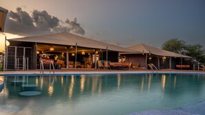 Un espace piscine avec des chaises longues et des parasols, un bar avec des sièges, et un espace extérieur couvert.