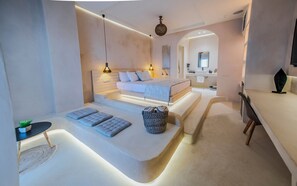 A modern bedroom with a built-in desk, a large bed with a headboard, and a bathroom visible through an archway. - Salida Del Sol Santorini  (Santorini)
