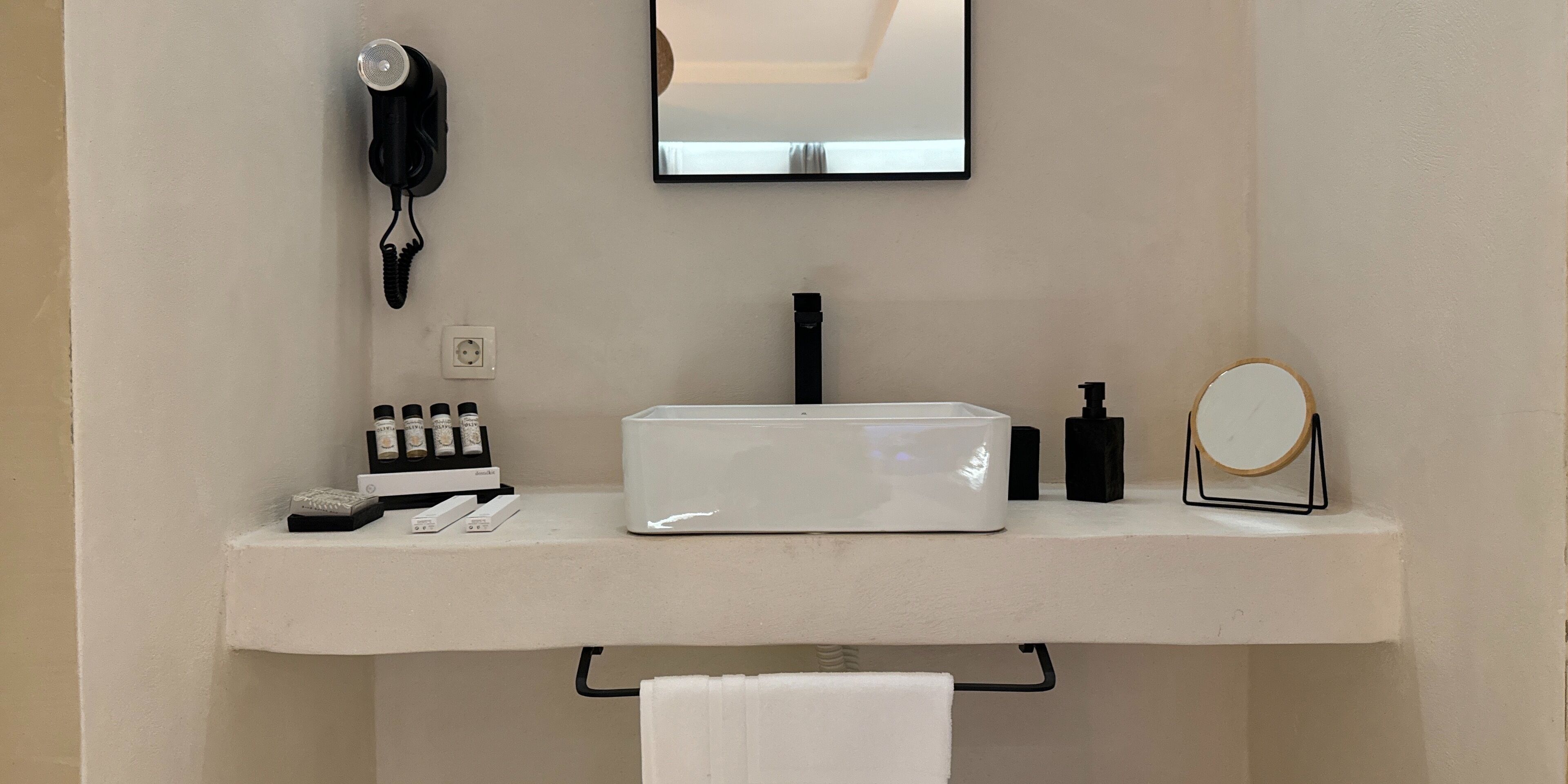 Un baño con tocador blanco, secador de pelo, espejo y artículos de aseo.