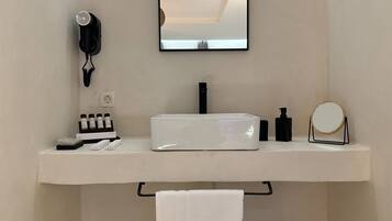 Un baño con tocador blanco, secador de pelo, espejo y artículos de aseo.