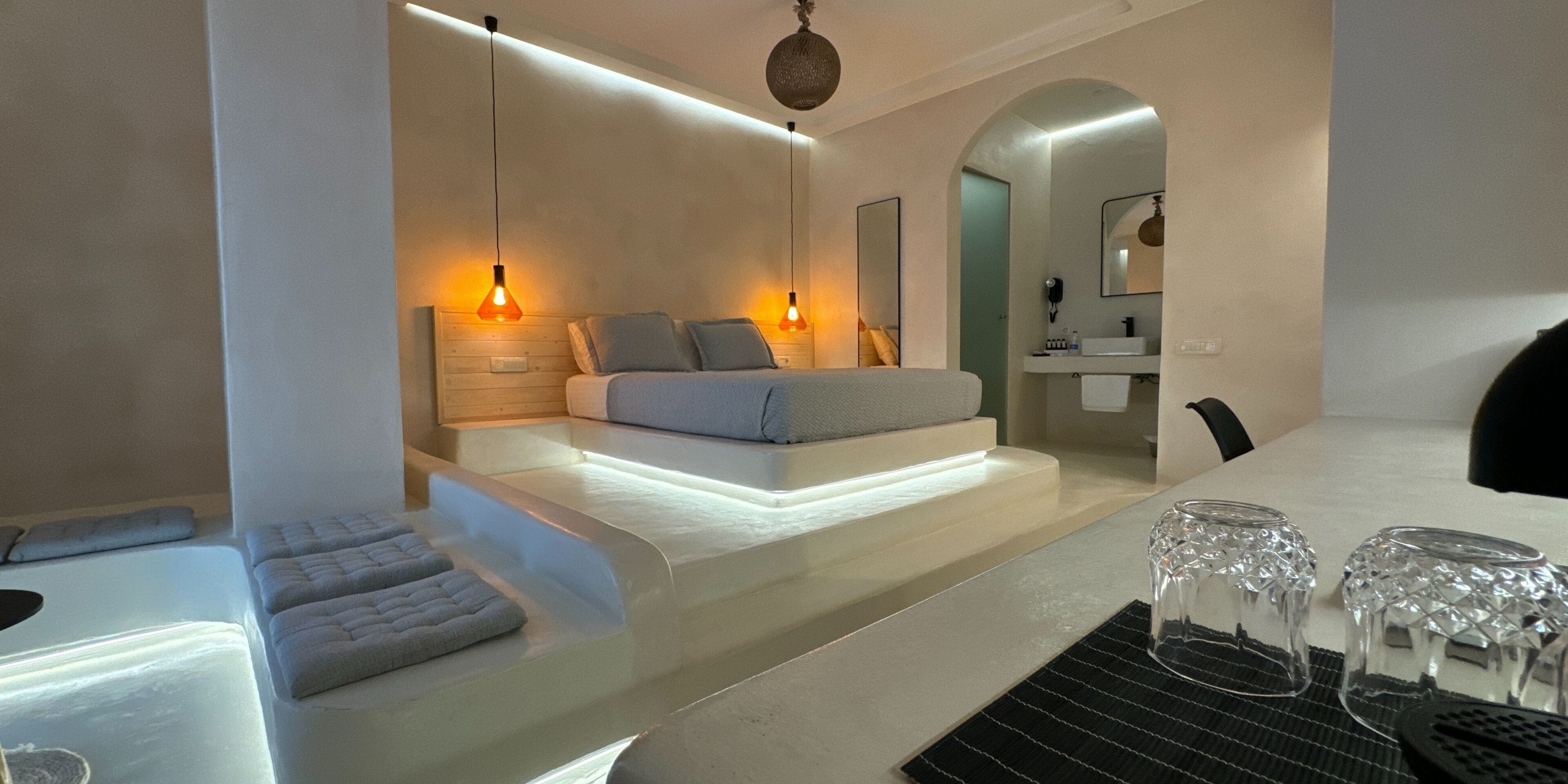A modern bedroom with a bed, bedside tables, and a bathroom visible through an archway.