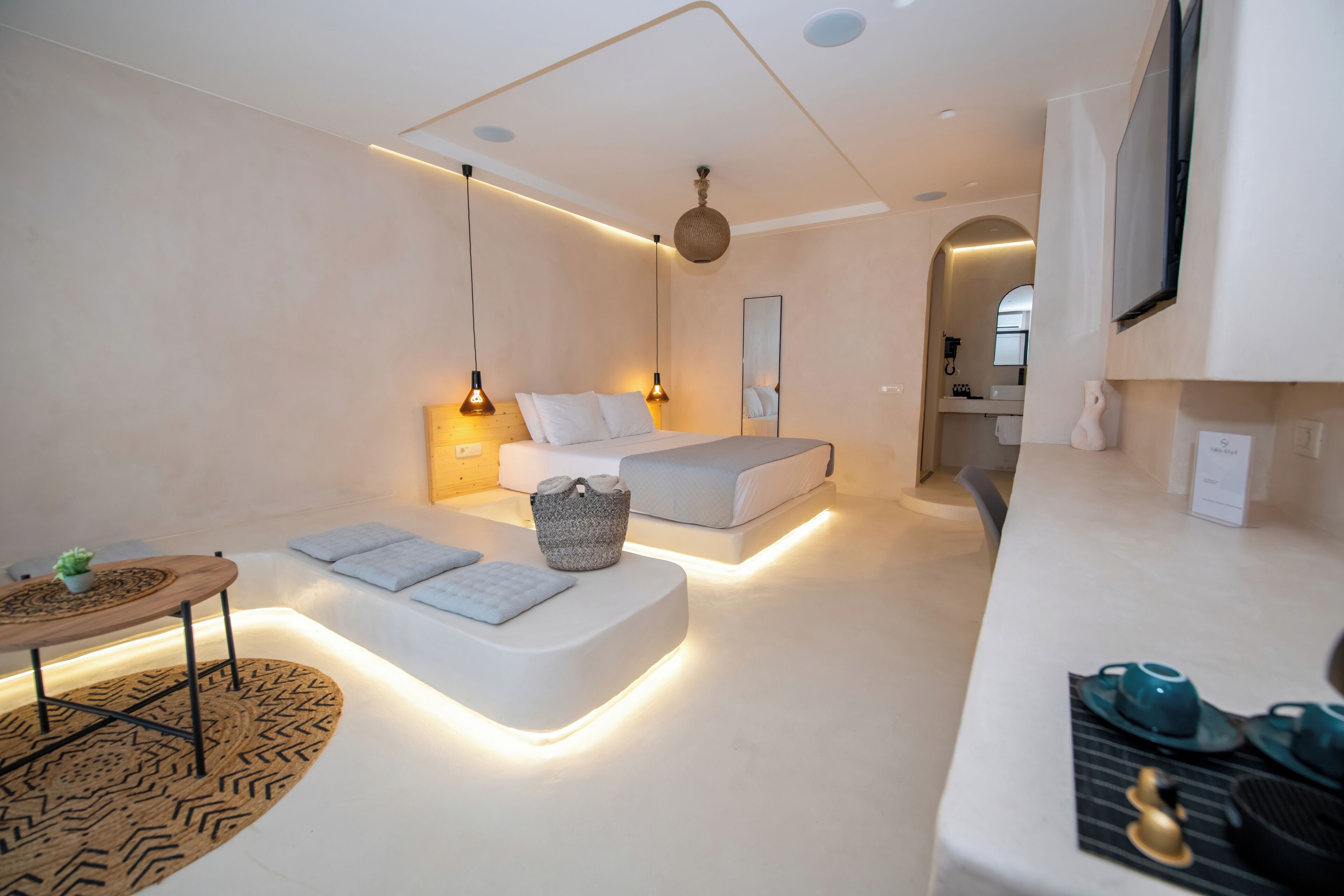 Een moderne hotelkamer met een bed, nachtkastje en een klein zithoekje met vloerkleed.