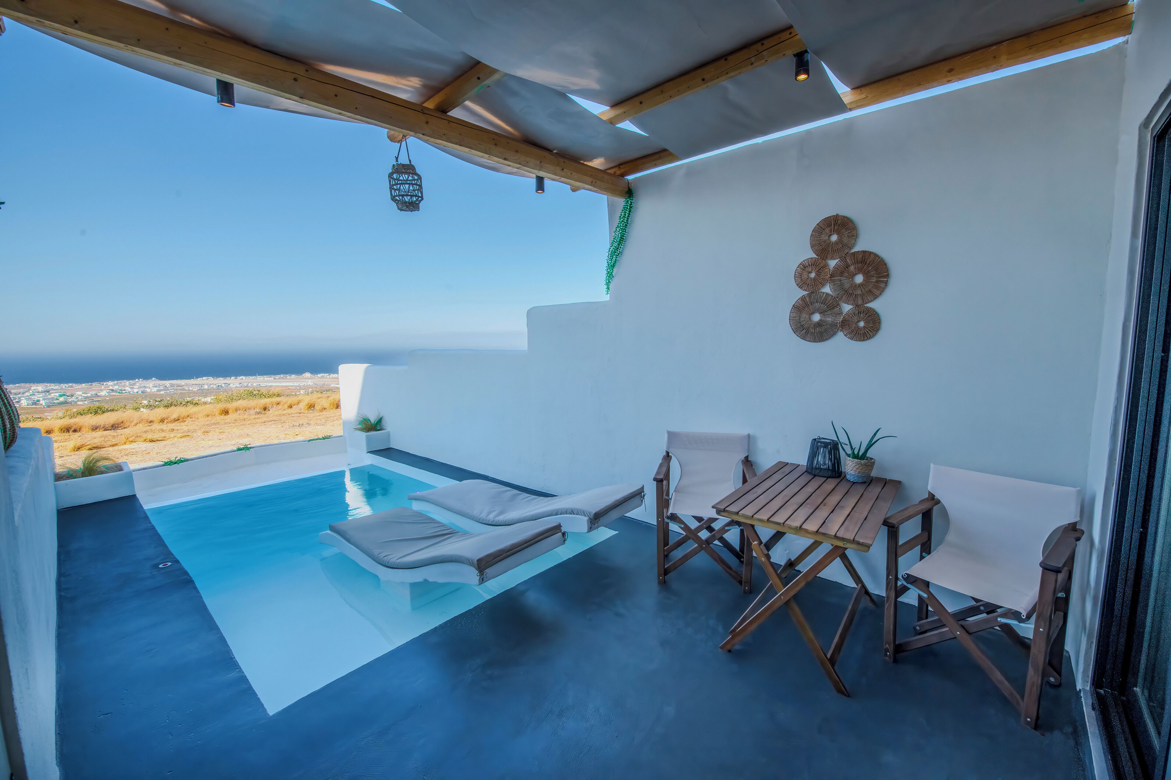 A modern outdoor pool area with a view of the ocean, wooden furniture, and decorative wall art.