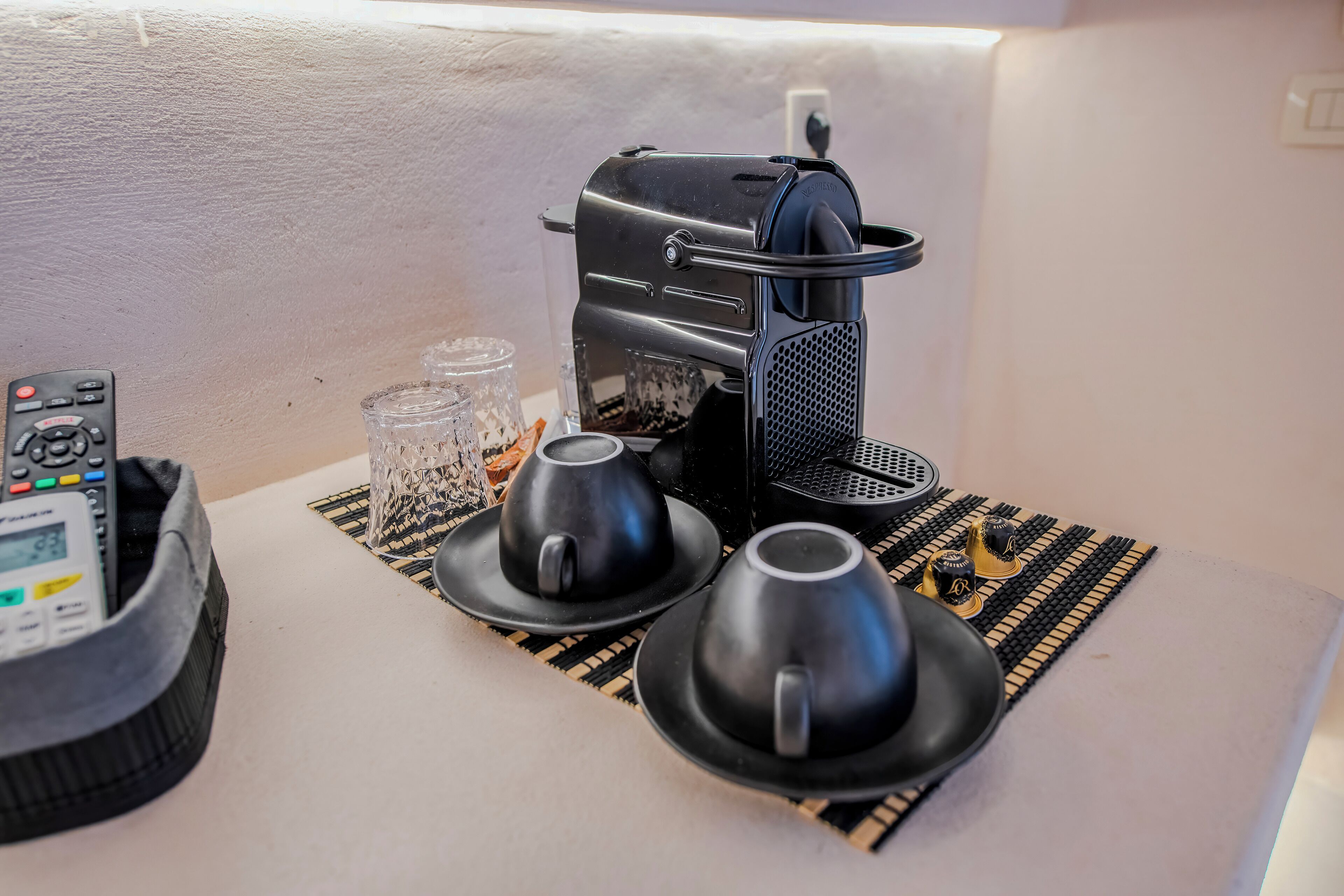 A coffee maker, two cups, and a remote control on a table.