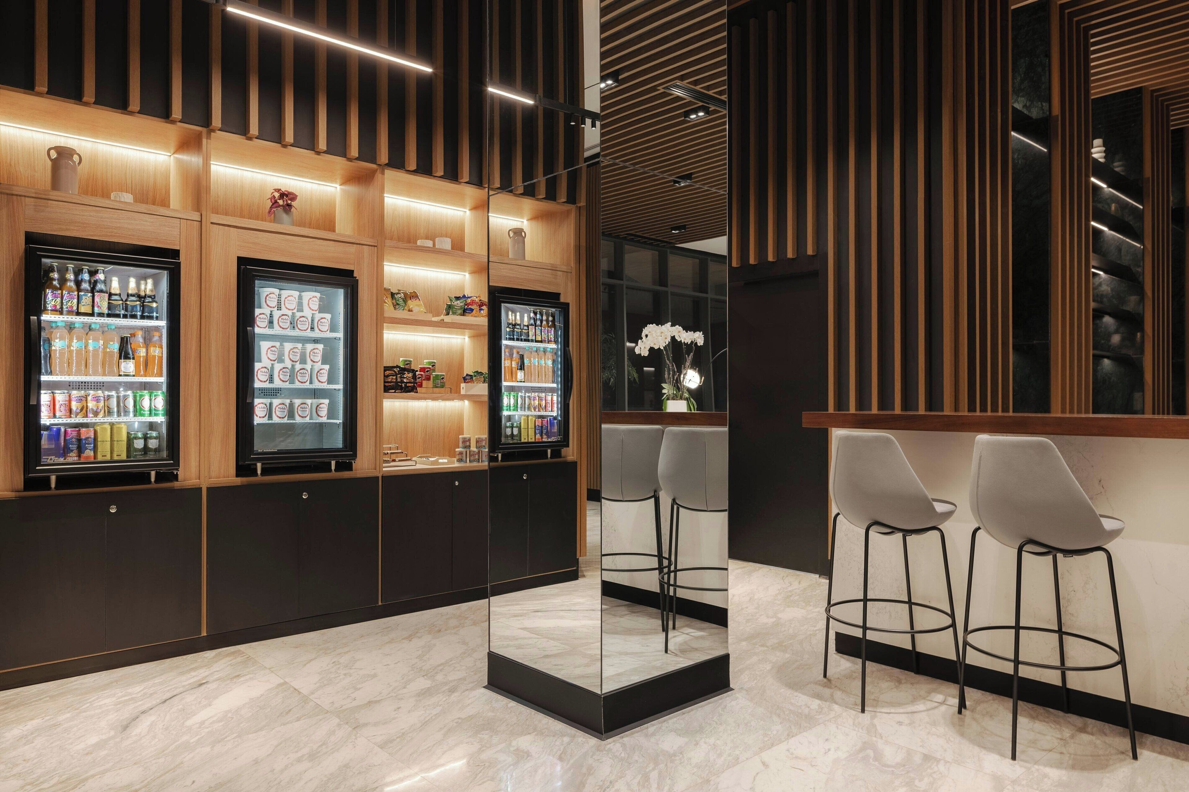 A modern bar area with a marble floor, wooden paneling, and a refrigerated display case.