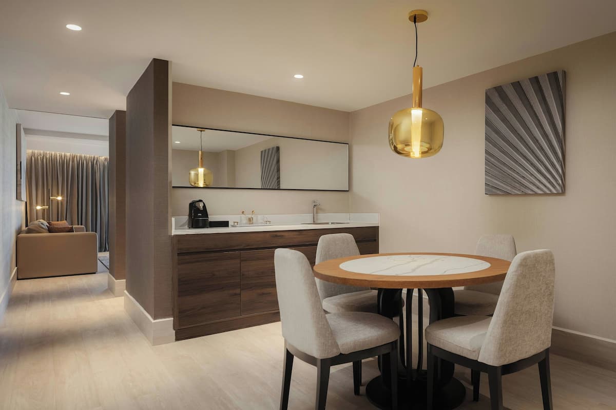 A modern dining area with a round table and four chairs, a large mirror, and a pendant light.