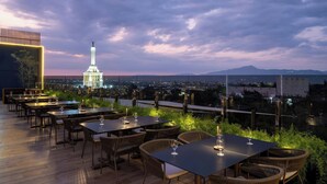An outdoor dining area with tables and chairs, overlooking a cityscape and a prominent tower. - AC Hotel Santiago de los Caballeros (Santiago de los Caballeros)