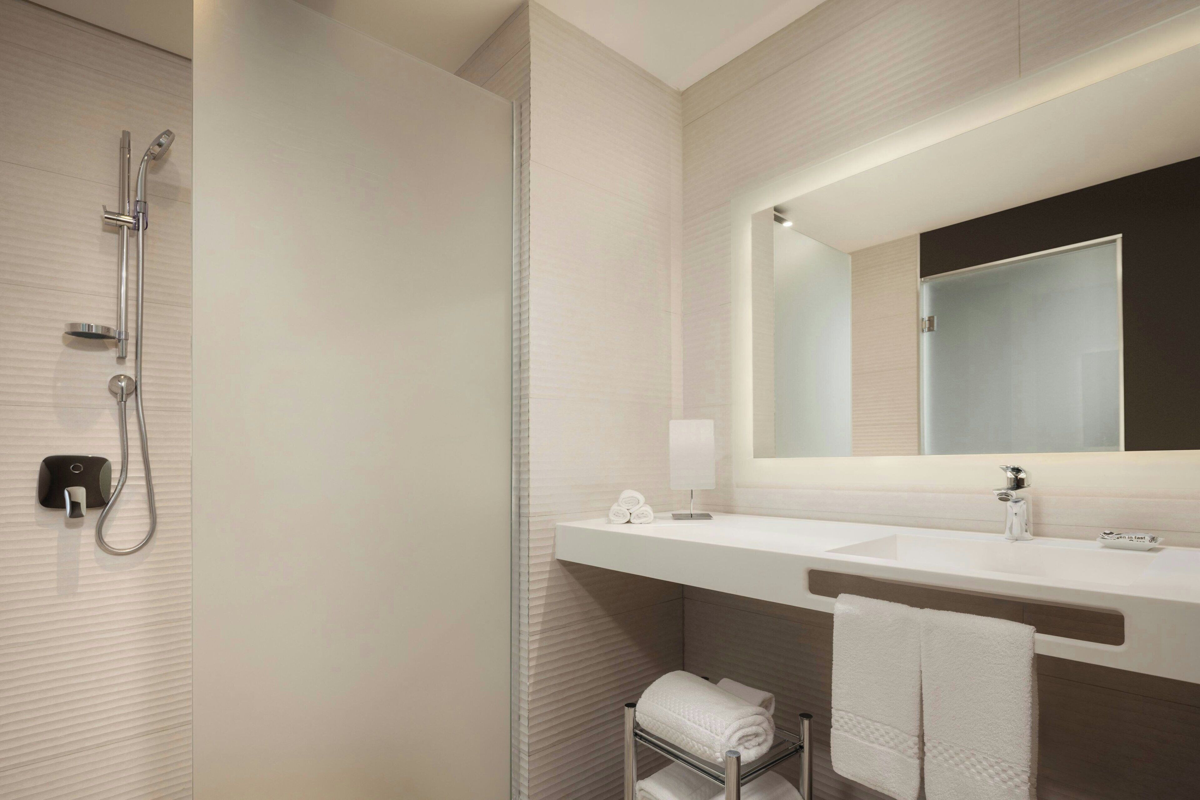 Un baño moderno con cabina de ducha de vidrio, tocador blanco con espejo y toallas dobladas con cuidado.